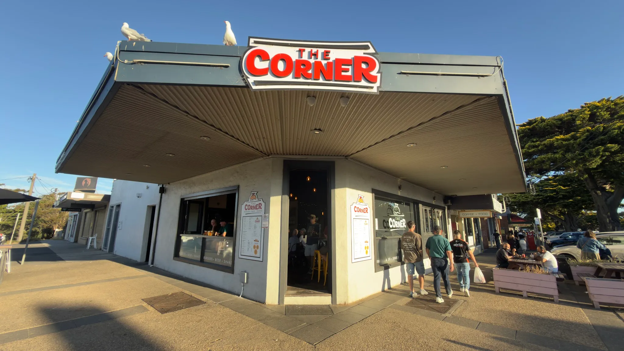 The Corner burger bar exterior at golden hour with its bold red sign, corner location, and people approaching the entrance
