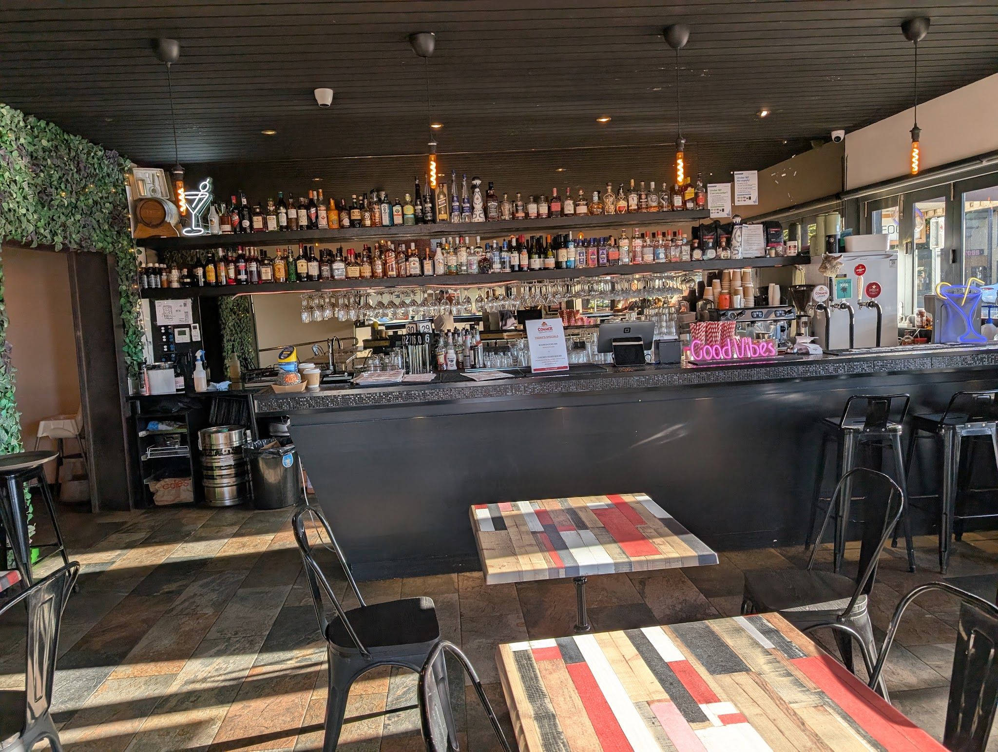 The Corner bar interior showing a fully stocked spirits wall, pendant lights, and colourful patchwork tables
