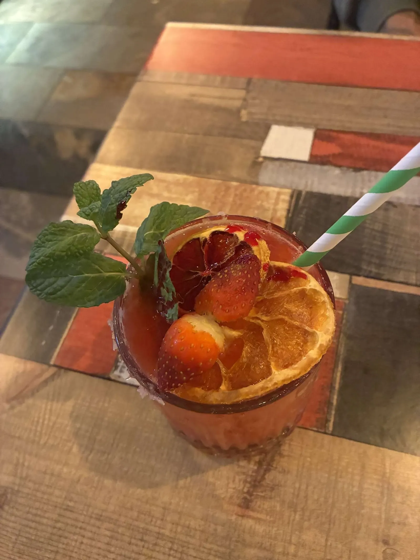 Craft cocktail with blood orange, strawberry, and mint garnish on The Corner's signature patchwork table