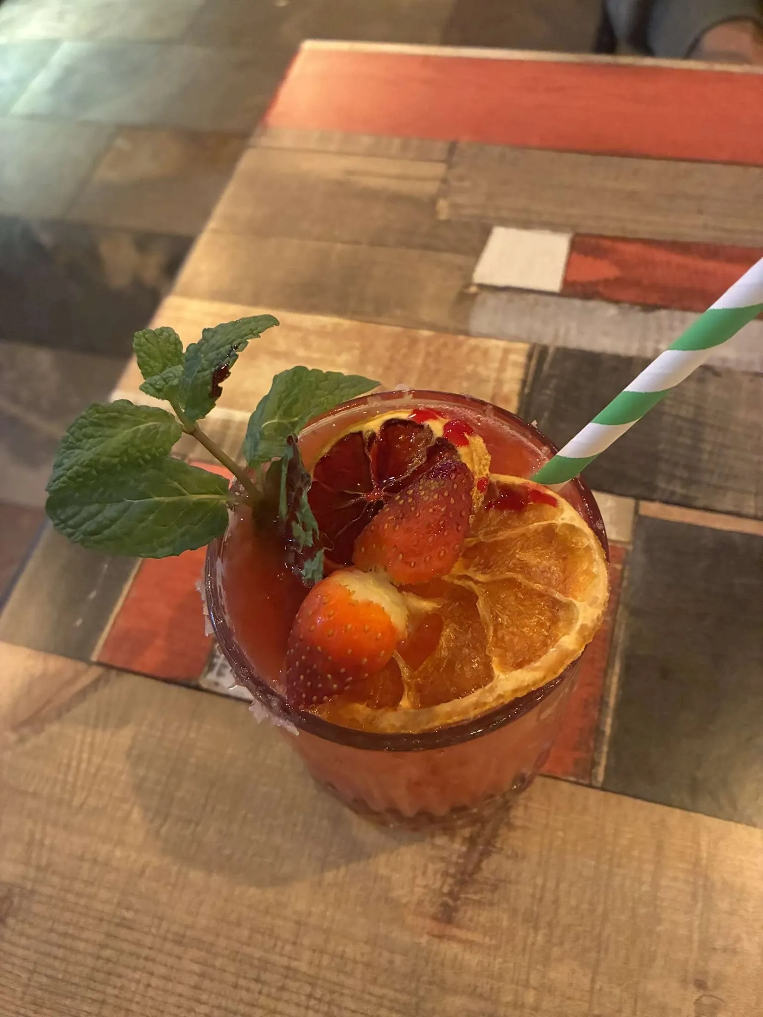 Craft cocktail with blood orange, strawberry, and mint garnish on The Corner's signature patchwork table