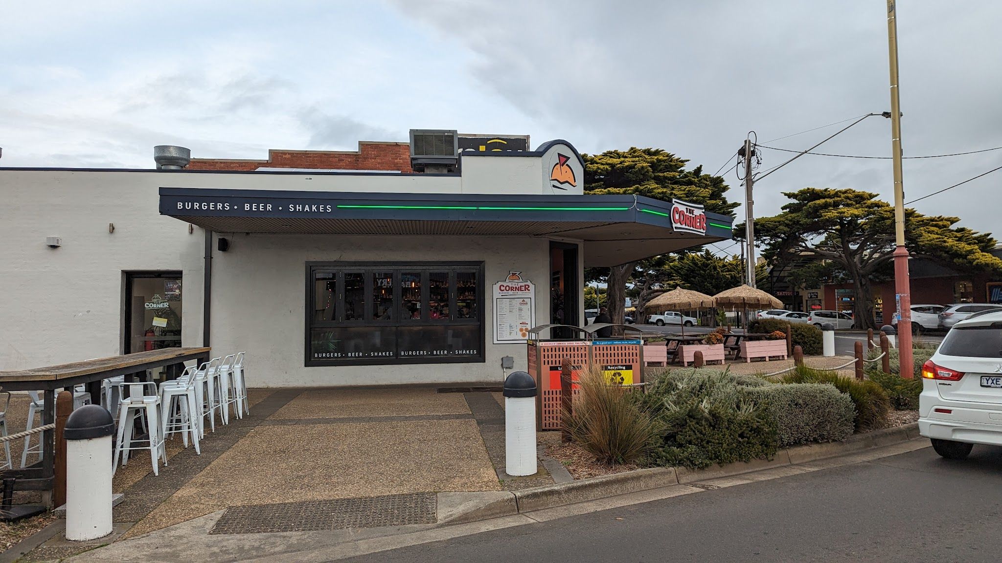 The Corner exterior on an overcast day showing outdoor seating, Burgers Beer Shakes signage, and corner location
