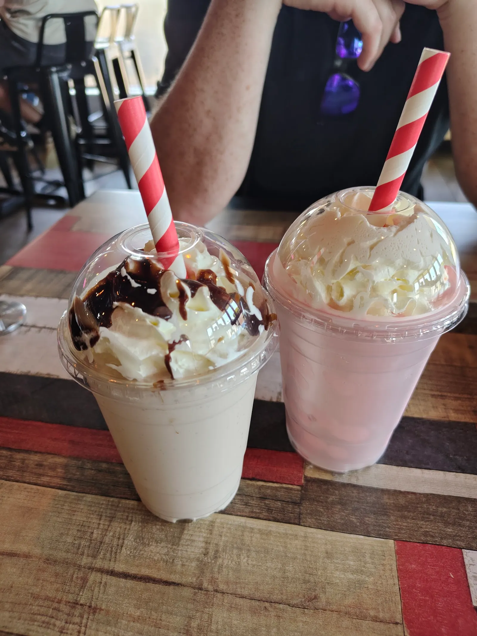 Two thick shakes — chocolate and strawberry — with whipped cream and striped straws on The Corner's patchwork table