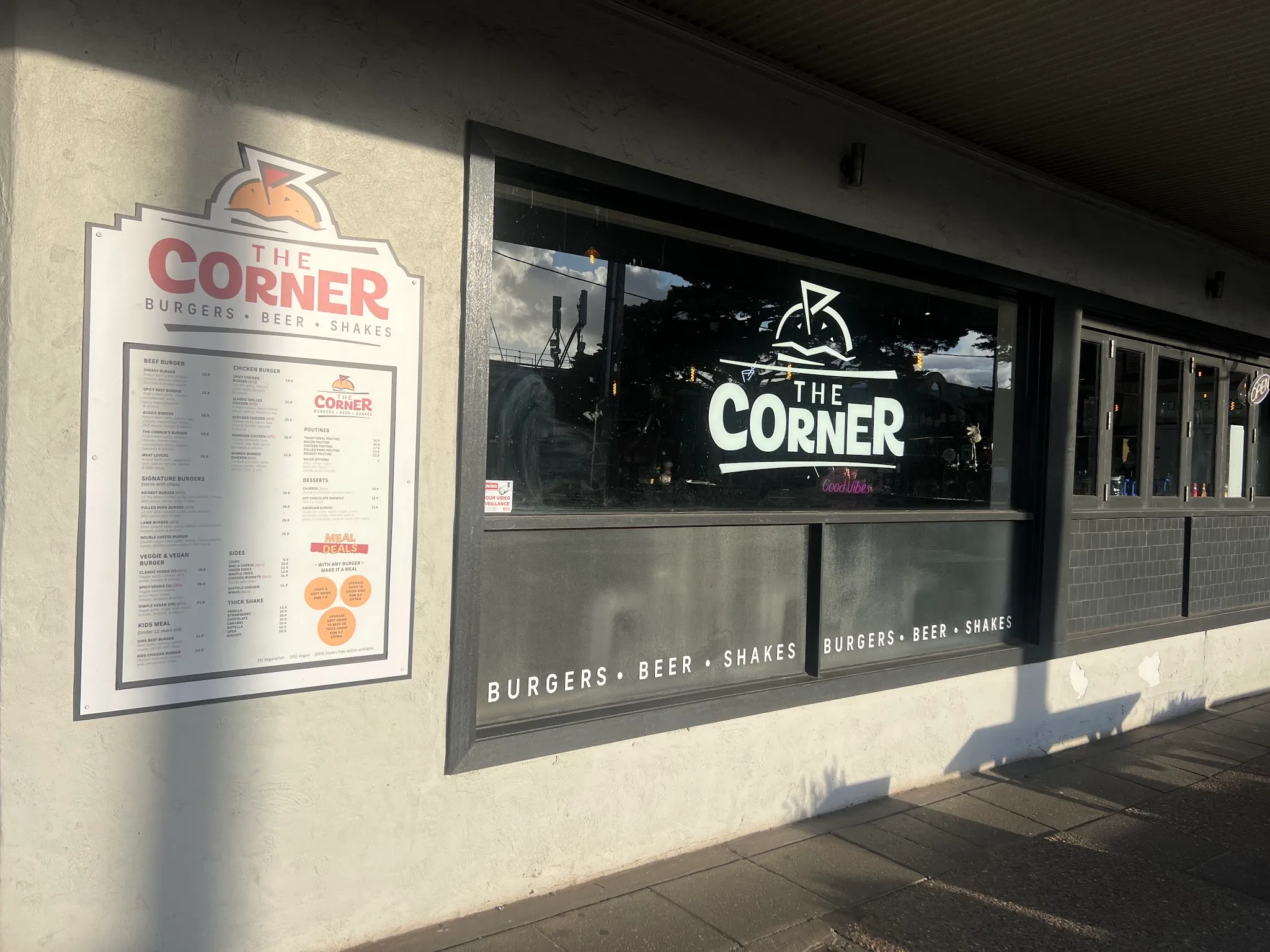 The Corner exterior showing the posted menu board, logo window decal and Burgers Beer Shakes signage