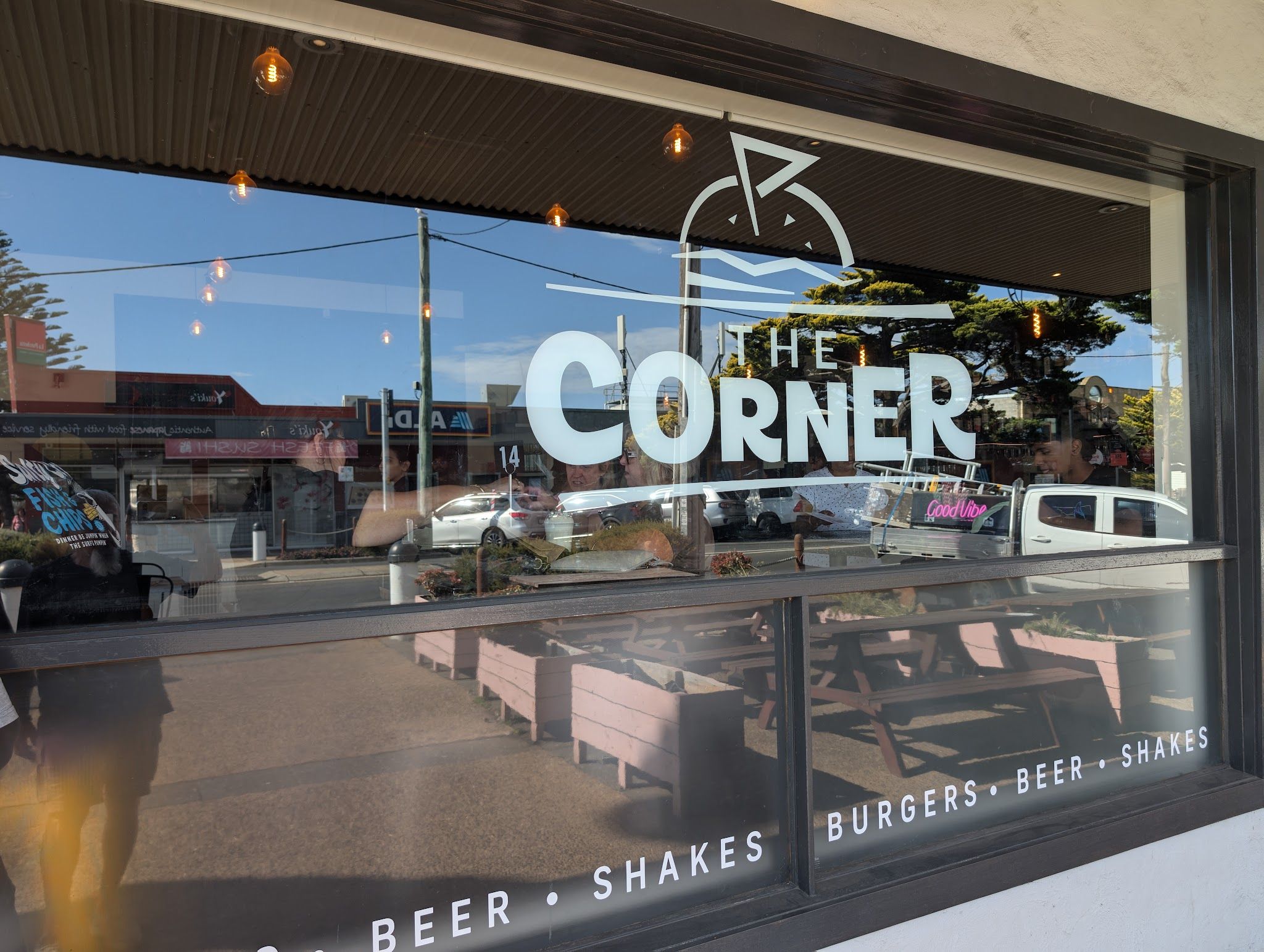 The Corner main window with white logo decal and pink outdoor bench seating