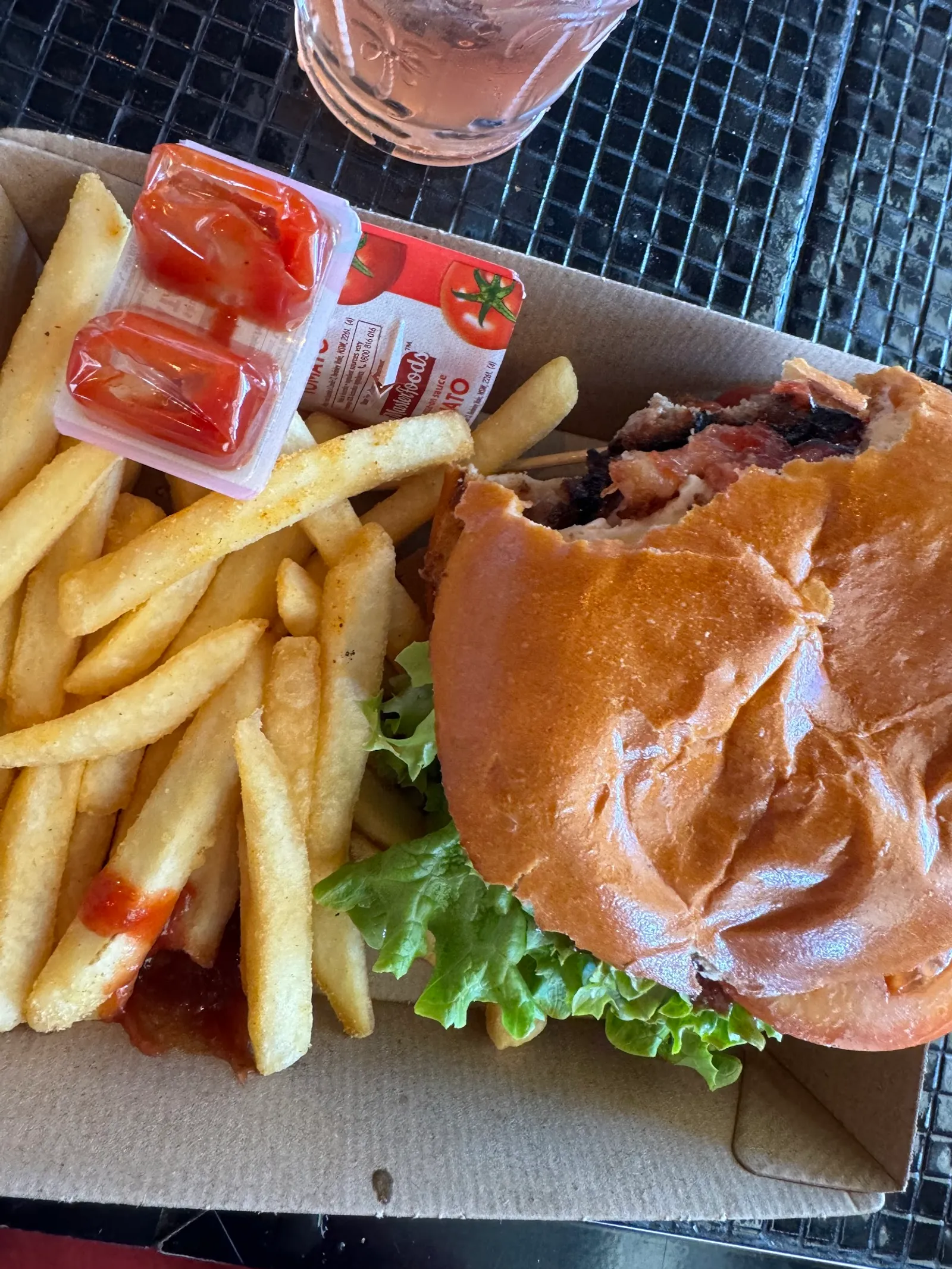 Burger and chips in a takeaway box with sauce packets on an outdoor table at The Corner