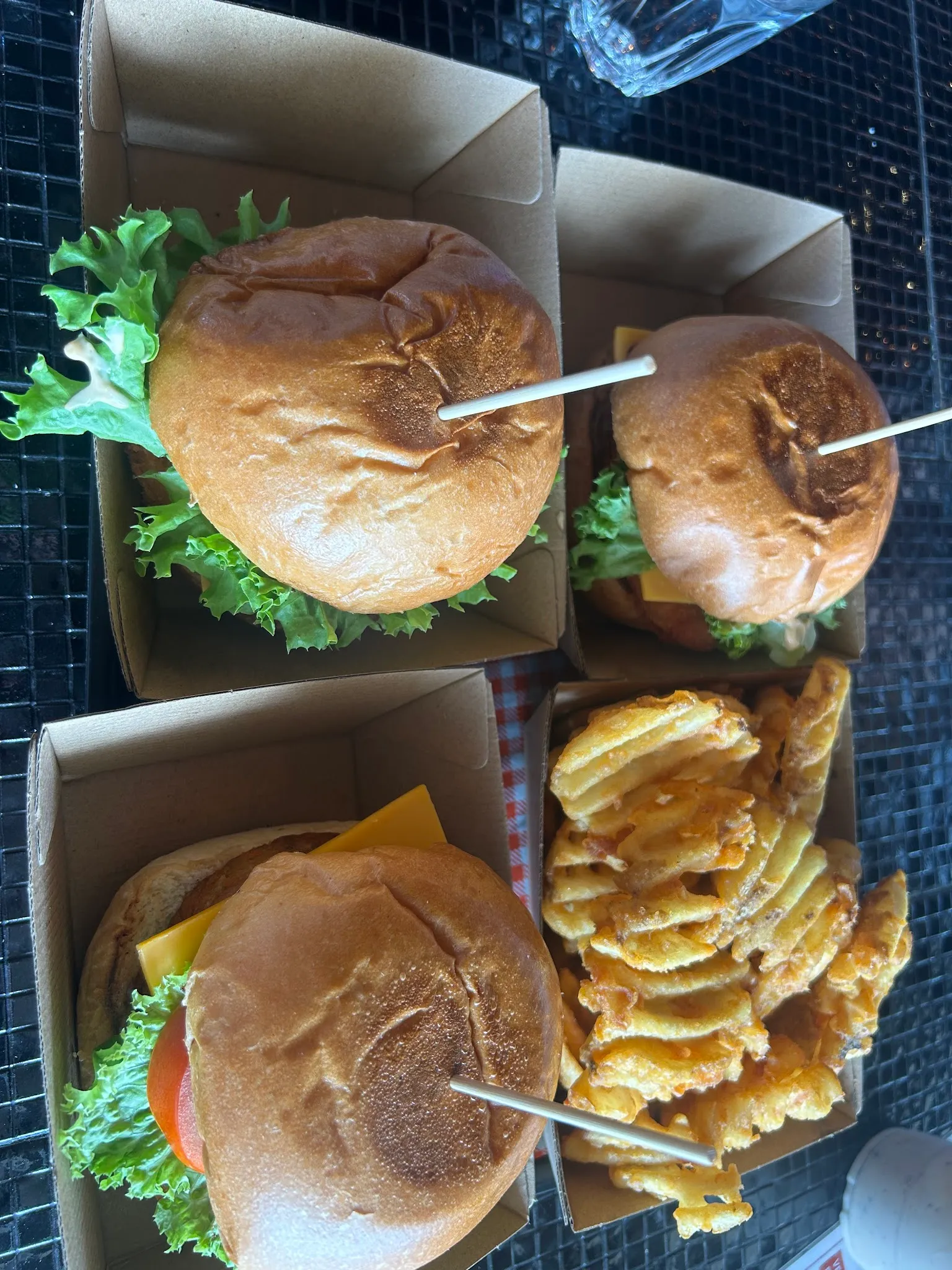 Four burgers in takeaway boxes with waffle fries from above at The Corner